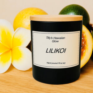 Tilly's Hawaiian Glow Lilikoi 10 oz hand-poured black soy candle with wooden lid, surrounded by whole and sliced passion fruit and yellow plumeria flowers.