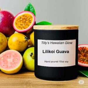 Tilly's Hawaiian Glow Lilikoi Guava 10 oz hand-poured black soy candle with wooden lid, next to a pile of whole and sliced lilikoi (passion fruit) and guavas.