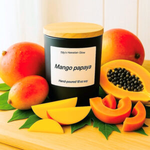 Tilly's Hawaiian Glow Mango Papaya 10 oz hand-poured black soy candle with wooden lid, surrounded by whole mangoes, whole and sliced papayas, and green leaves.