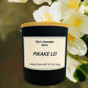 Tilly's Hawaiian Glow Pikake Lei 10 oz hand-poured black soy candle with wooden lid, against a soft-focus background of white pikake (jasmine) flowers.