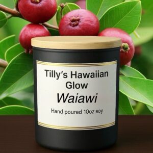 Tilly's Hawaiian Glow Waiawi 10 oz hand-poured black soy candle with wooden lid, against a background of red waiawi (strawberry guava) fruits on a branch with green leaves.